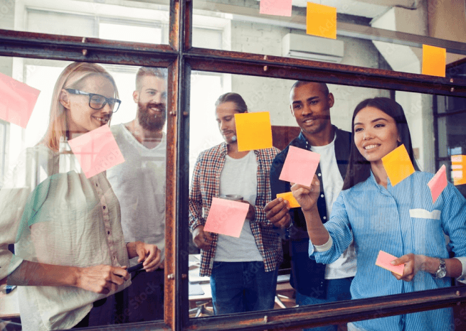 Picture of colleagues putting up and analyzing post-it notes on a clear glass wall.