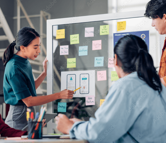 Picture of woman presenting information on a whiteboard between two ideations of an app.